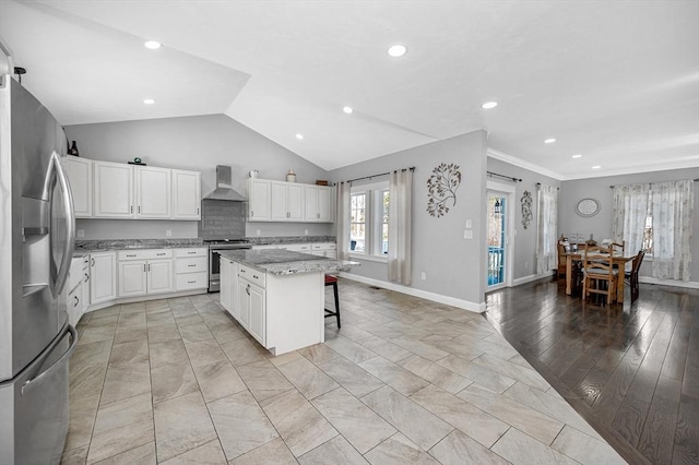 kitchen featuring wall chimney exhaust hood, a kitchen island, a breakfast bar area, stainless steel appliances, and white cabinetry