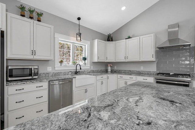 kitchen with pendant lighting, stainless steel appliances, lofted ceiling, white cabinetry, and wall chimney range hood