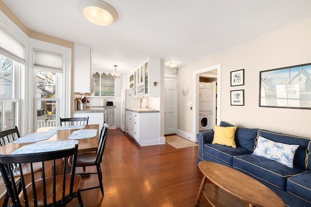 dining space with stacked washer and clothes dryer, sink, an inviting chandelier, and dark hardwood / wood-style flooring