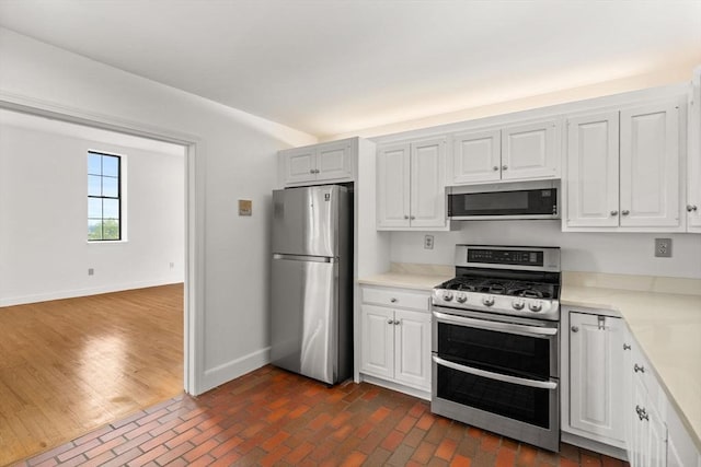 227 Summit Unit W207, Brookline, MA 02446 - kitchen featuring stainless steel appliances, baseboards, light countertops, brick patterned floors, and white cabinetry
