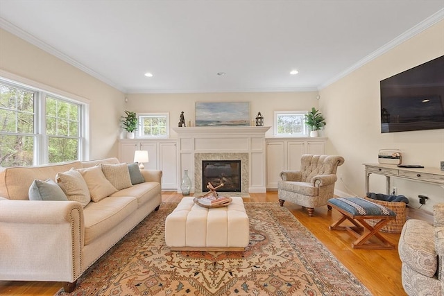 living room featuring light wood-type flooring, crown molding, a premium fireplace, and recessed lighting