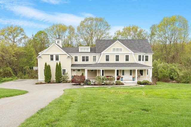 shingle-style home with a porch, roof with shingles, a front yard, and driveway