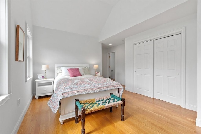 bedroom featuring light wood finished floors, lofted ceiling, baseboards, and a closet