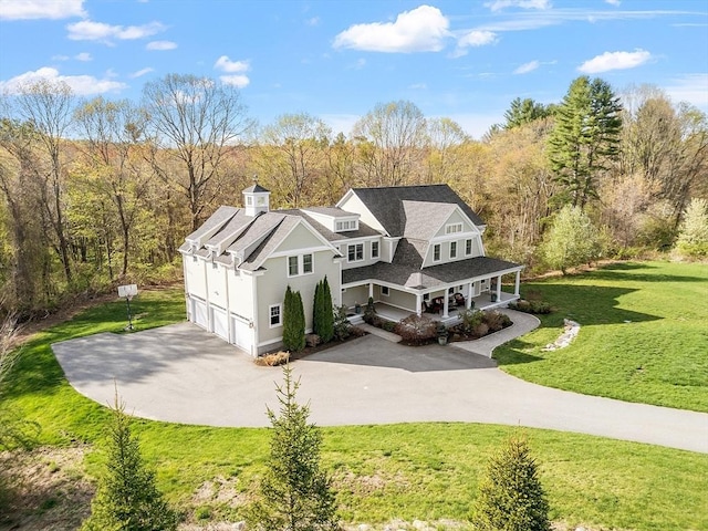 view of front of property with covered porch, driveway, a front lawn, an attached garage, and a wooded view