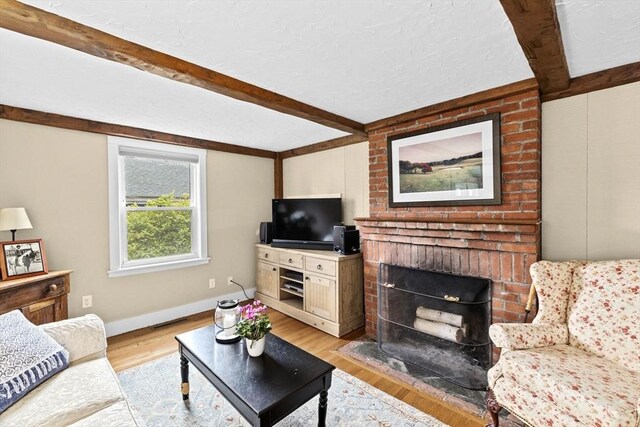 23 Garden Rd, Scituate, MA 02066 - living area with beam ceiling, light wood-type flooring, a textured ceiling, and a brick fireplace