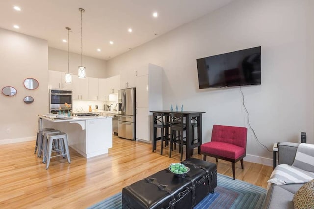 living area with recessed lighting, a high ceiling, light wood-type flooring, and baseboards