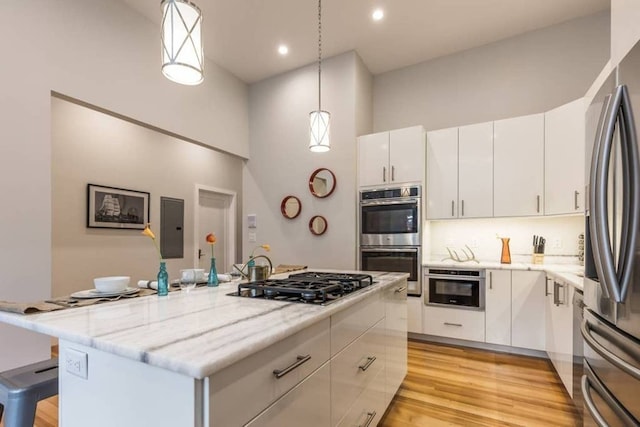 kitchen featuring light wood-type flooring, pendant lighting, a kitchen island, appliances with stainless steel finishes, and white cabinets