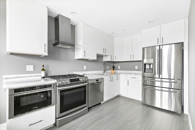 kitchen featuring recessed lighting, a sink, stainless steel appliances, white cabinetry, and wall chimney range hood