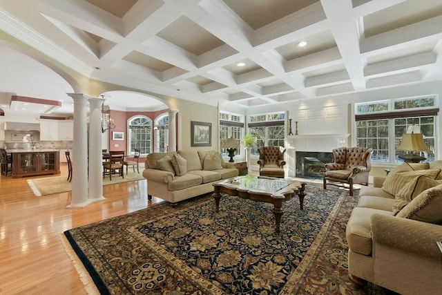 living room with arched walkways, a fireplace, light wood-type flooring, beam ceiling, and decorative columns