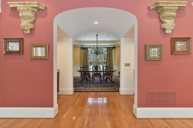 corridor with arched walkways, baseboards, visible vents, and light wood finished floors