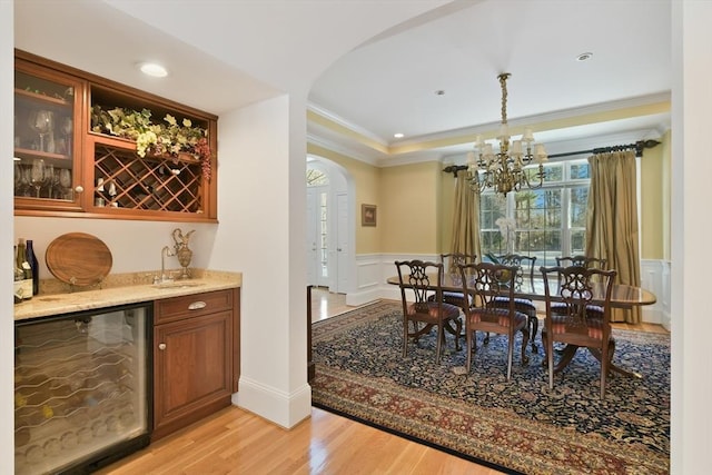 dining area with arched walkways, wine cooler, a wainscoted wall, ornamental molding, and light wood finished floors