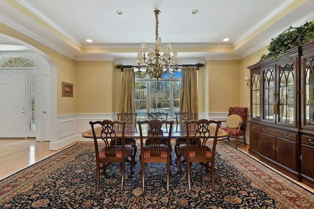 dining space featuring arched walkways, a raised ceiling, a wainscoted wall, wood finished floors, and an inviting chandelier