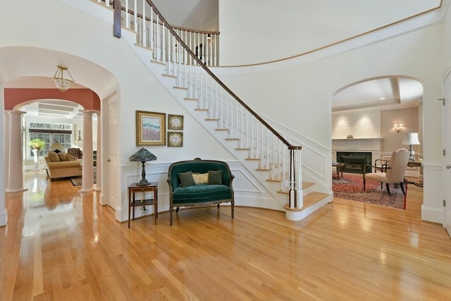 entrance foyer with decorative columns, wood finished floors, stairs, a fireplace, and a decorative wall