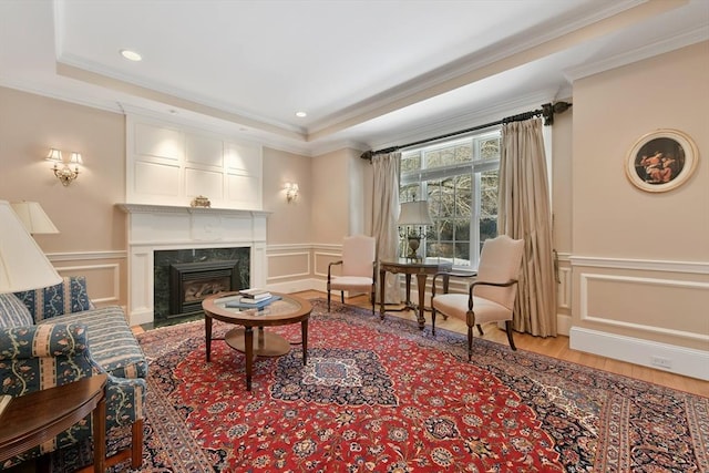 sitting room with ornamental molding, a fireplace, a raised ceiling, and a decorative wall