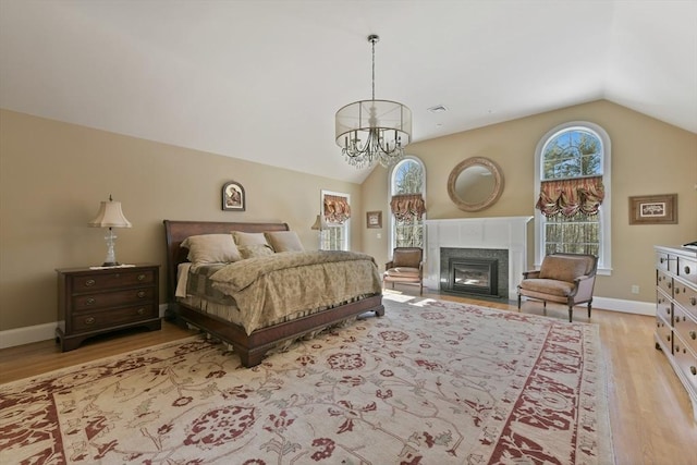 bedroom with a fireplace with flush hearth, lofted ceiling, light wood-style flooring, and baseboards