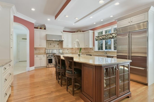 kitchen with arched walkways, light wood-style flooring, a kitchen island, a sink, and high end appliances