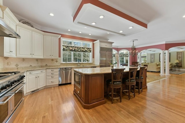 kitchen featuring built in appliances, arched walkways, a kitchen island, a sink, and decorative columns