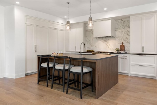 kitchen featuring pendant lighting, white cabinetry, an island with sink, sink, and light hardwood / wood-style flooring