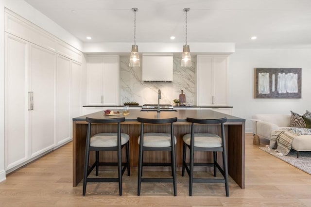 bar featuring sink, decorative backsplash, light hardwood / wood-style floors, and white cabinets