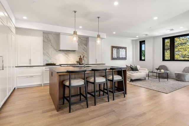 kitchen featuring pendant lighting, white cabinetry, a kitchen bar, a center island with sink, and light wood-type flooring