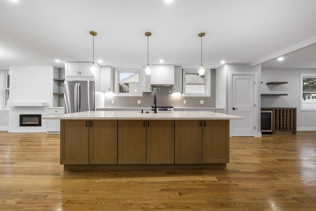 kitchen featuring a large island, light wood-style flooring, light countertops, freestanding refrigerator, and a sink