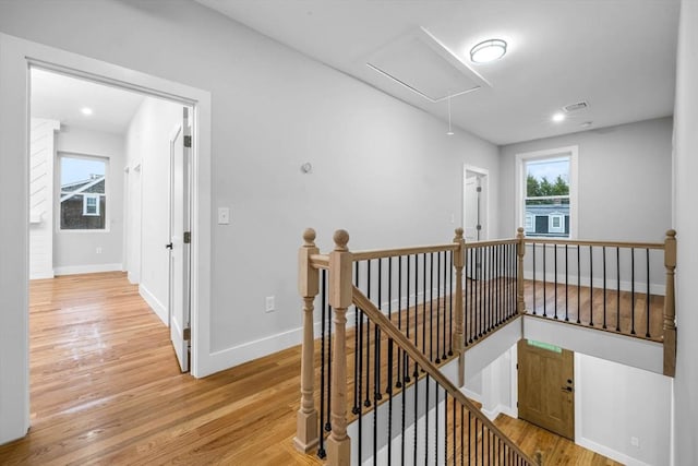 hall with light wood-style floors, attic access, baseboards, and an upstairs landing