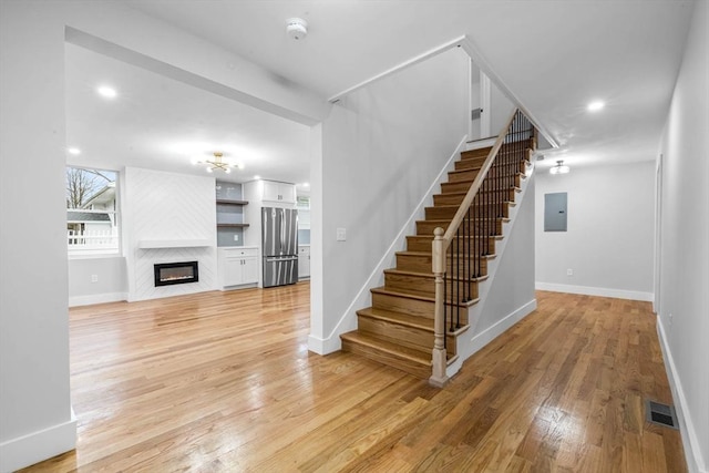 stairs featuring visible vents, baseboards, hardwood / wood-style floors, and a glass covered fireplace