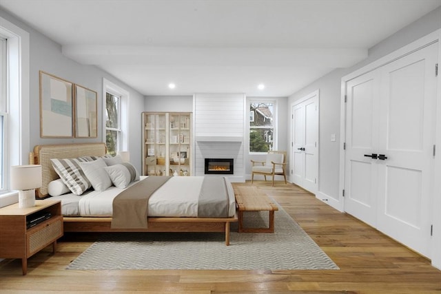 bedroom featuring two closets, light wood finished floors, a fireplace, and recessed lighting
