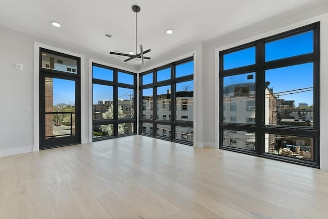 empty room with an inviting chandelier, visible vents, wood finished floors, baseboards, and recessed lighting