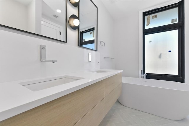 full bathroom with double vanity, a freestanding bath, a sink, and visible vents