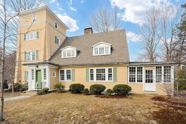 view of front of house with a shingled roof, a front yard, a chimney, and stucco siding