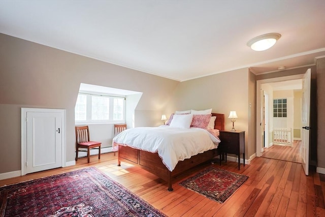 bedroom featuring a baseboard heating unit, light wood-style floors, and baseboards