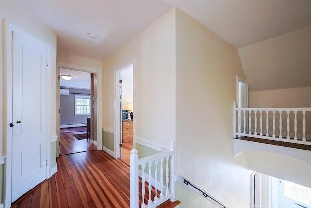 corridor with dark wood-style flooring, lofted ceiling, a baseboard heating unit, an upstairs landing, and baseboards