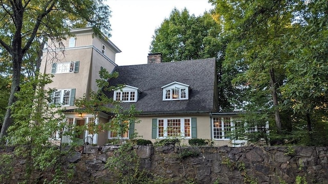 view of front facade with roof with shingles, a chimney, and stucco siding