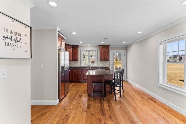 kitchen featuring baseboards, ornamental molding, a kitchen bar, light wood-type flooring, and a center island