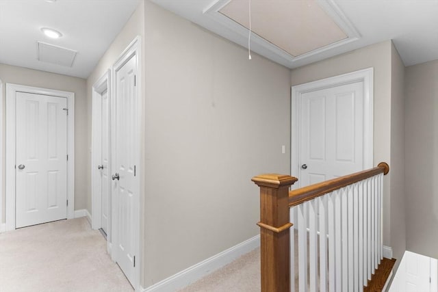 corridor with an upstairs landing, light colored carpet, attic access, and baseboards