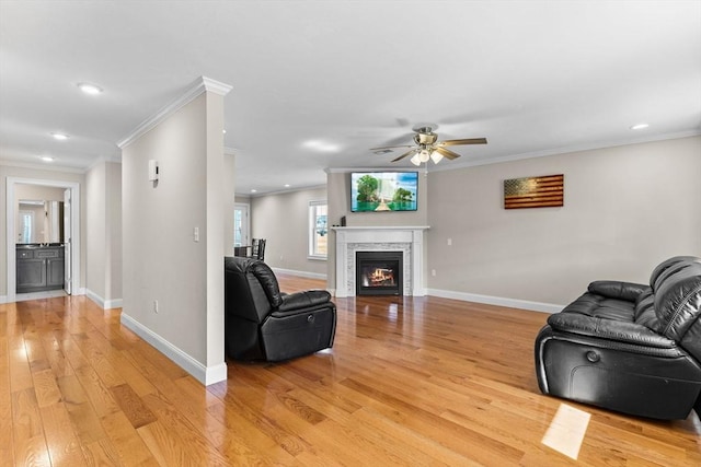 living area with a glass covered fireplace, light wood-style flooring, crown molding, and baseboards