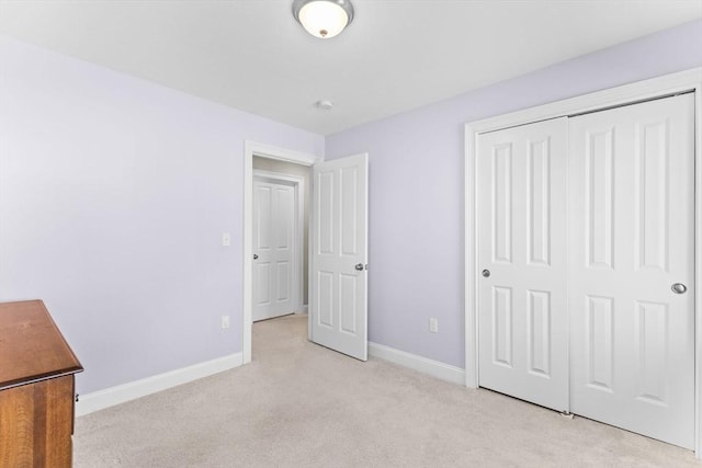 unfurnished bedroom featuring light carpet, a closet, and baseboards