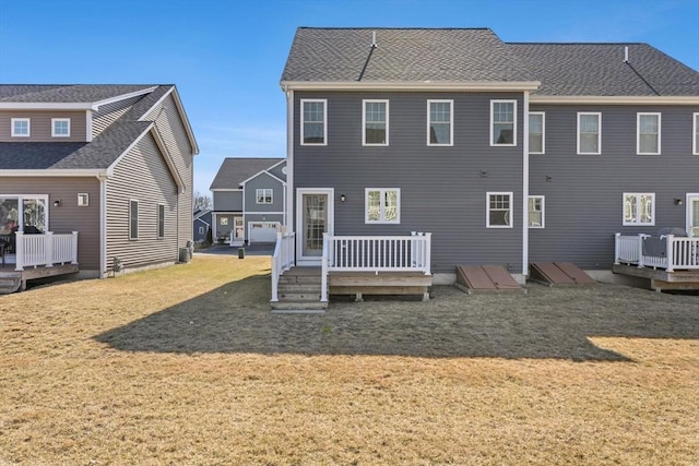 rear view of property featuring a shingled roof, a lawn, and a wooden deck