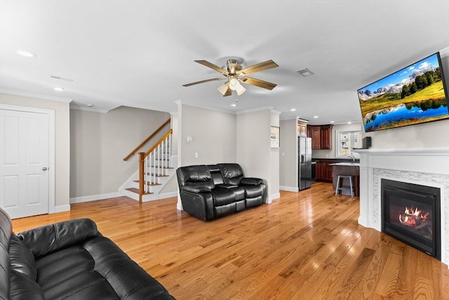 living room with stairway, light wood-style flooring, crown molding, and a glass covered fireplace