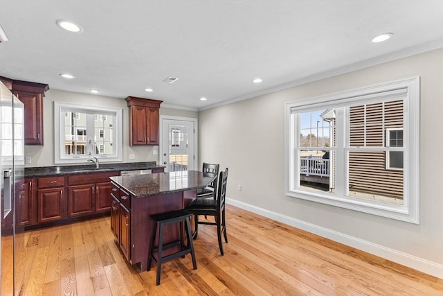 kitchen with a kitchen breakfast bar, a center island, dark stone counters, light wood finished floors, and baseboards