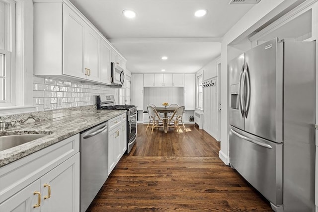 kitchen featuring backsplash, light stone countertops, white cabinets, stainless steel appliances, and dark wood-type flooring