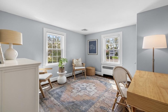 office area featuring baseboards, visible vents, radiator heating unit, and wood finished floors