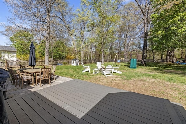 wooden terrace featuring a fenced backyard, a playground, a storage unit, a yard, and outdoor dining space