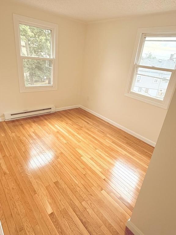 212 Fountain St Unit A, Framingham, MA 01702 - spare room featuring a baseboard radiator, light wood finished floors, plenty of natural light, and a textured ceiling