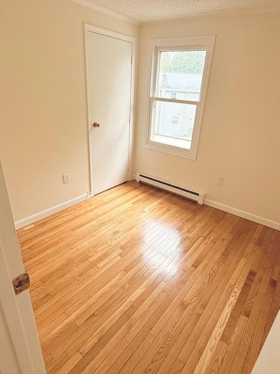 212 Fountain St Unit A, Framingham, MA 01702 - empty room with a baseboard radiator, light wood finished floors, and a textured ceiling