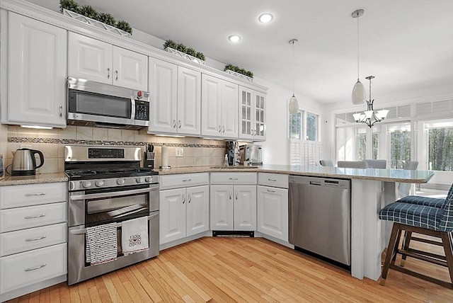 kitchen featuring stainless steel appliances, a breakfast bar, white cabinets, and decorative light fixtures