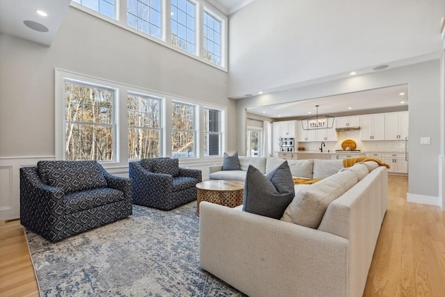 living room featuring a towering ceiling, sink, and light hardwood / wood-style flooring