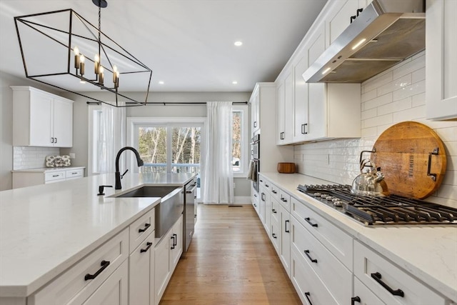 kitchen featuring white cabinetry, sink, range hood, and stainless steel gas cooktop