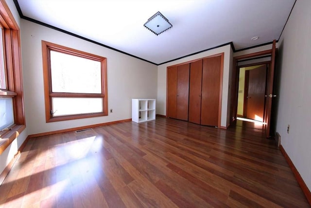 unfurnished bedroom with a closet, dark wood-type flooring, and crown molding